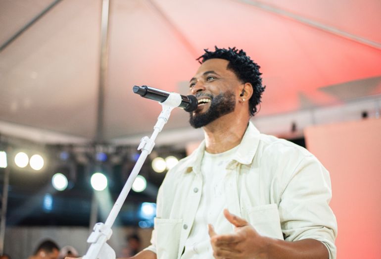 Julio Sereno tocando um instrumento (ou cantando) durante a gravação de seu audiovisual em um cenário que remete a um quintal festivo, com público ao fundo.