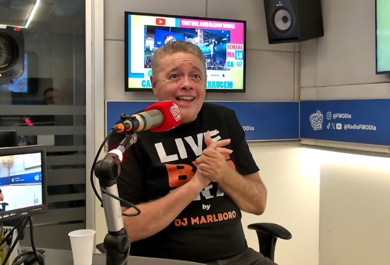 Foto do DJ Malboro usando fones de ouvido e falando ao microfone dentro de um estúdio de gravação